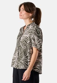 Short-sleeve blouse in green and cream zebra pattern, featuring a button-up front, collared neck, and relaxed fit with gathered sleeves.
