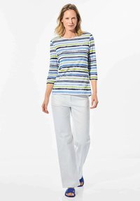 Gestreept shirt in lichtblauw, groen en marineblauw; driekwartmouwen. Gecombineerd met witte recht-toe-recht-aan broek en blauwe sandalen.