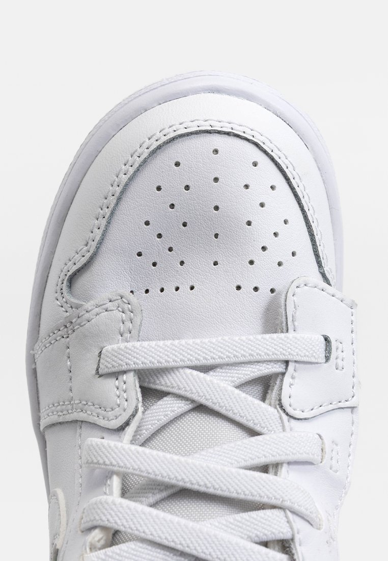 Zapatilla deportiva blanca con parte superior de cuero liso, puntera perforada para transpirabilidad, cordones planos y detalles cosidos a lo largo de los bordes.