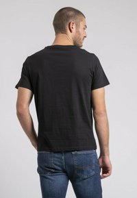 Chemise noire en coton à manches courtes et col rond, présentée de dos, assortie à un jean en denim bleu avec des poches arrière.