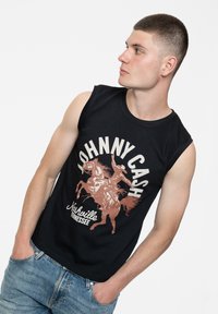 Black sleeveless cotton shirt featuring a graphic print of a cowboy on a horse with the text "Johnny Cash" and "Nashville Tennessee" in cream and brown.