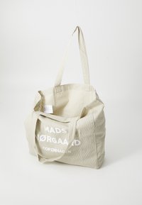 Borsa tote a righe beige con testo bianco, dotata di due lunghe maniglie e di un ampio interno aperto. Realizzata in materiale tessile.