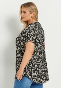 Top negro con estampado de flores en blanco y naranja, con mangas cortas, un corte relajado y dobladillo redondeado. Llevado con vaqueros azules.