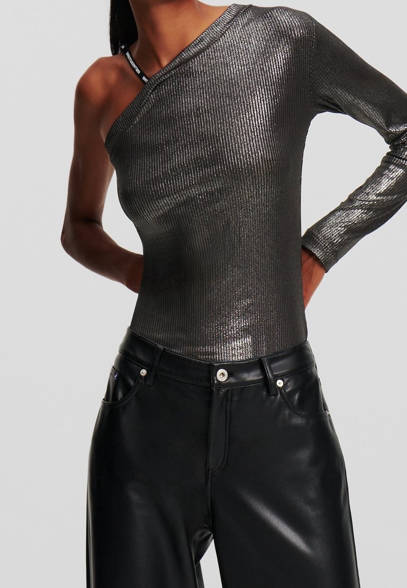 Haut métallique asymétrique à une épaule en tissu côtelé, avec une texture brillante. Associé à un pantalon en cuir noir taille haute avec poches et garnitures argentées.