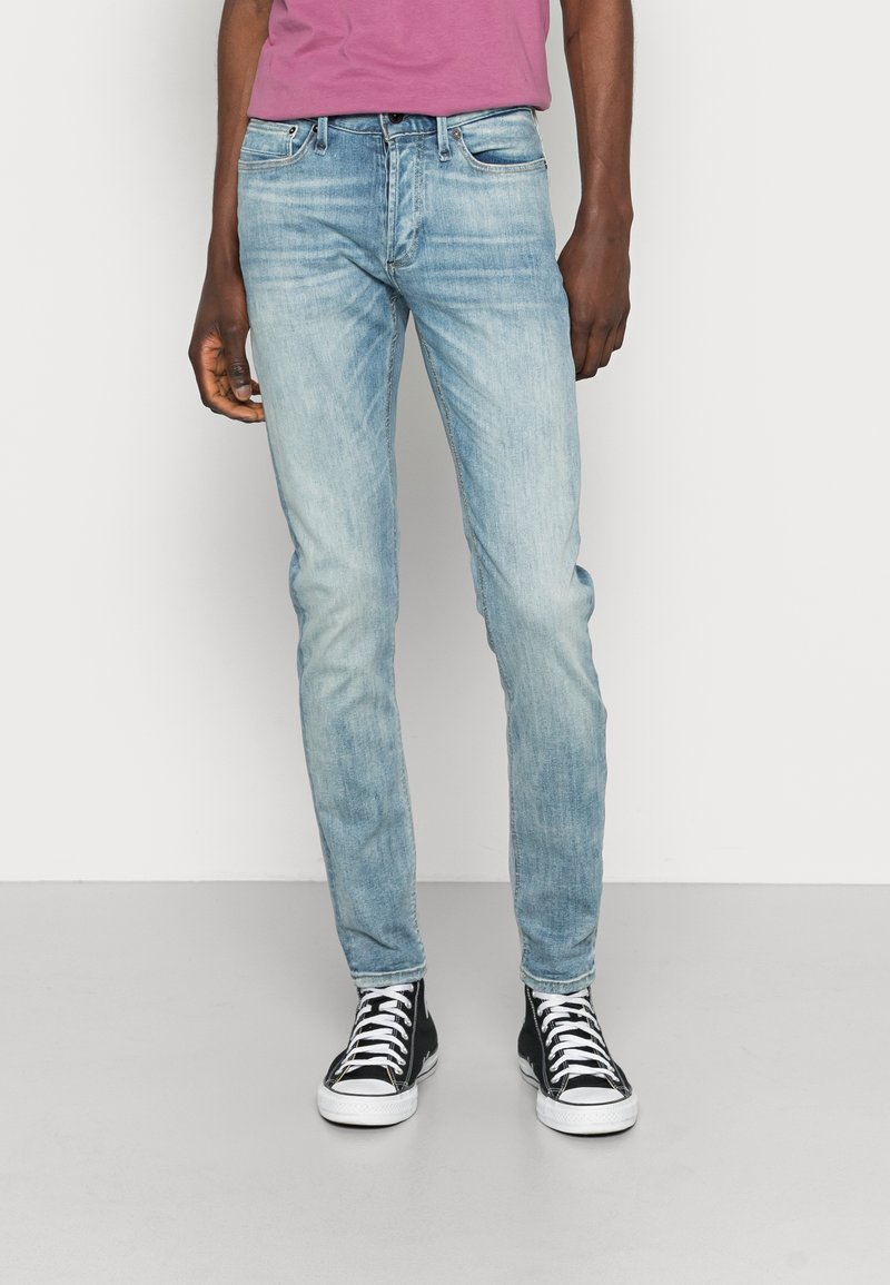 Vaqueros skinny de color azul claro con un acabado desgastado, cinco bolsillos, pasantes para cinturón y un leve estiramiento. Llevados con zapatillas negras de caña alta.