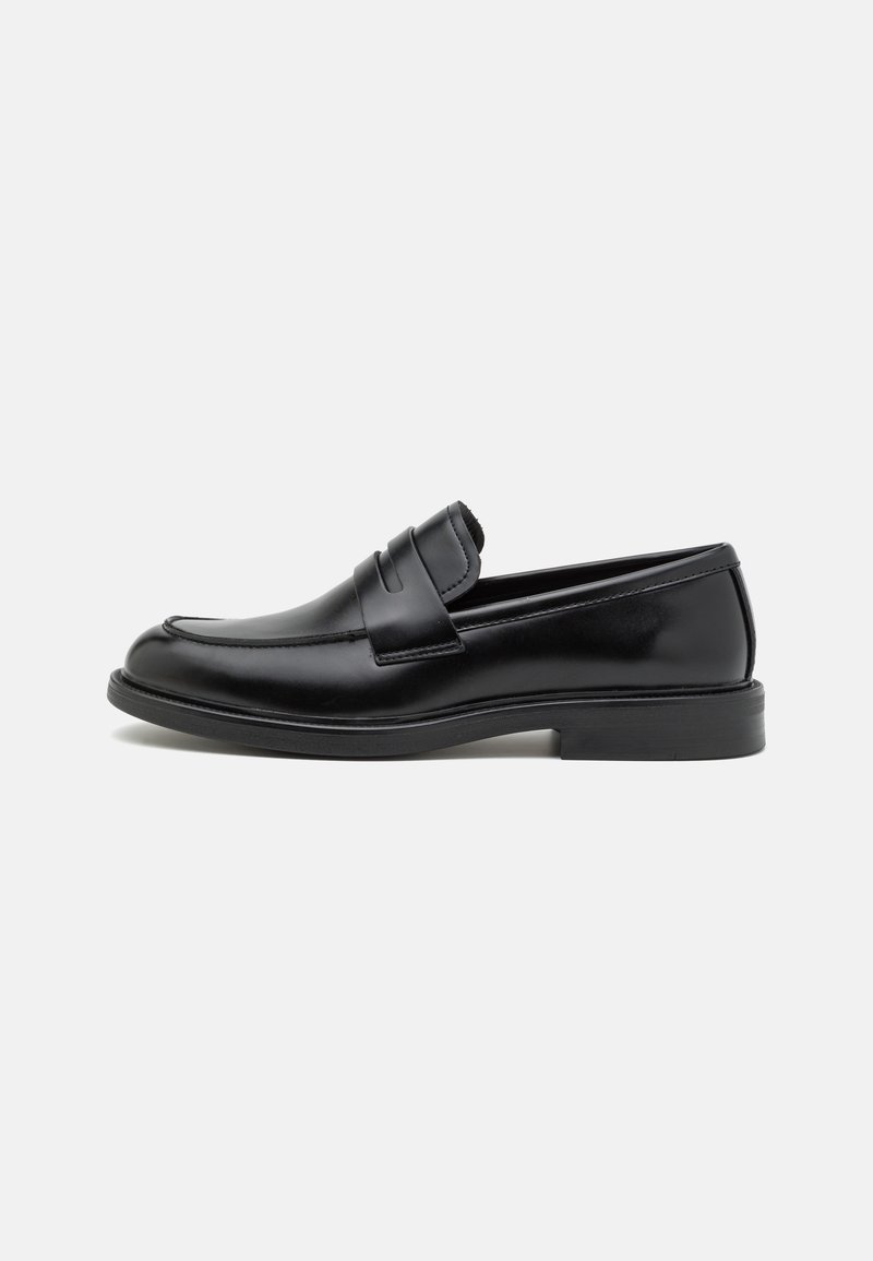 Mocasines de cuero negro con puntera redondeada, detalles cosidos en el empeine y una suela de goma plana para mayor tracción. Textura lisa en toda su superficie.