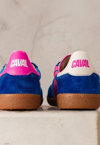 Paire de baskets en daim bleu avec semelles marron, languettes de talon roses et blanches, chacune étiquetée "CAVAL" en lettres grasses.