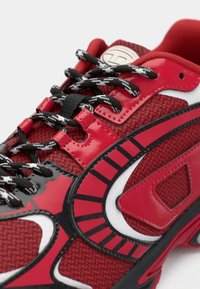 Red and black athletic shoe with patterned fabric, black-and-white laces, glossy overlays, and a padded collar.