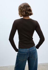 Top marrone a maniche lunghe aderente al corpo, abbinato a jeans blu in denim a vita alta con tasche posteriori. Tessuto liscio e design semplice.