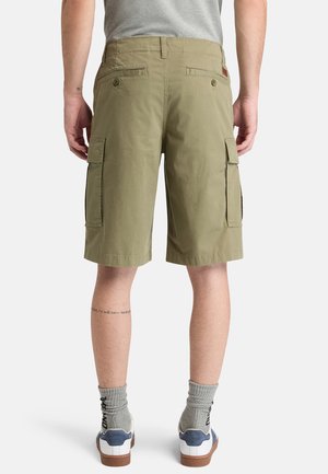 Mann, der khakifarbene Cargoshorts, graue Socken und weiße Turnschuhe trägt, von hinten vor weißem Hintergrund gezeigt.