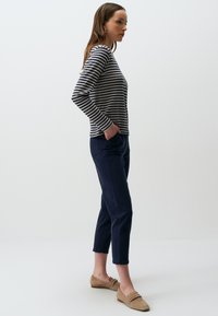 Gestreepte longsleeve top in marineblauw en crème, met een brede halslijn. Gecombineerd met donker marineblauwe cropped broek en beige instapschoenen.