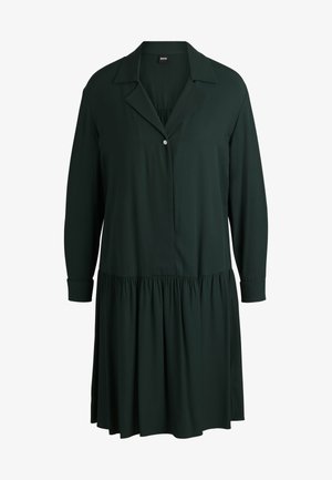 Robe longue à manches longues de couleur vert foncé en tissu lisse. Elle présente une patte de boutonnage, un col et une jupe à volants froncés.