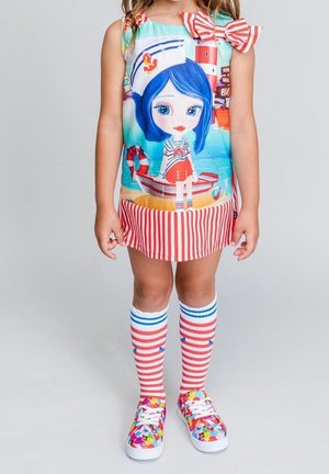 Stribet kjole med et farverigt trykt motiv med en figur. Hvide og røde knælange strømper samt blomstrede slip-on sko.