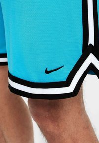 Μπλέ αθλητικοί σορτς με μαύρη και λευκή διακόσμηση, φορεμένοι στο πόδι ενός ατόμου, με ένα μικρό μαύρο λογότυπο Nike στην άκρη.