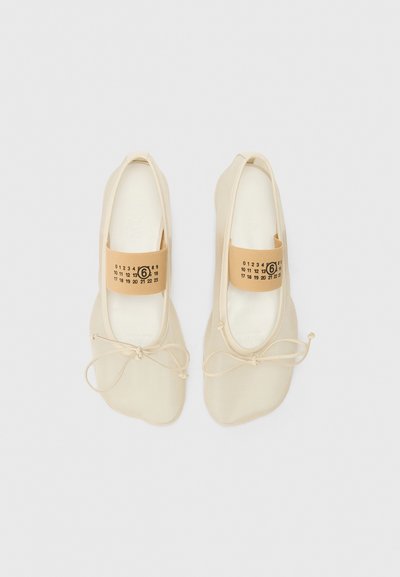 Beige ballet flats with a smooth material, rounded toe, light bow detail, and elastic strap featuring printed size and number accents.