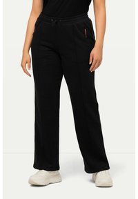 Černé tepláky vyrobené z měkké látky, s pasem na šňůrku a bočními zipovými kapsami s červenými detaily. Fitted design rovného střihu.