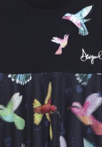 Kolorowe haftowane i drukowane kolibry z błyszczącymi detalami na czarnym tle, w towarzystwie stylizowanych kształtów serc i kursywnego tekstu.