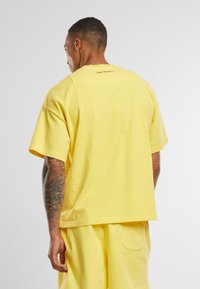 Yellow cotton t-shirt with short sleeves, oversized fit, crew neckline, and small text detail at the back. Smooth texture, casual design.