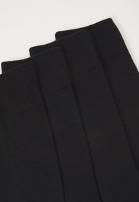 Sorte bomuldsstrømper med ribbet tekstur, der har et ensfarvet design og medium højde, samlet i et sæt af fire.