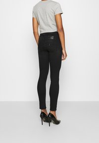 Vaqueros pitillo negros de cintura alta, con textura de denim suave y bolsillos traseros, combinados con una camiseta gris y tacones altos negros.