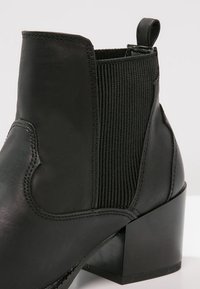 Stivaletto in pelle nera con pannelli laterali elasticizzati rigati, tacco a blocco e linguetta sul retro per facilitarne l'indossamento.
