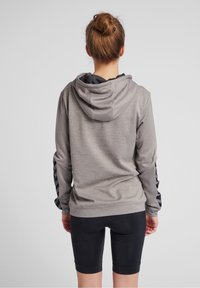 Huvtröja i grått med texturerad tyg, med svarta accentdetaljer på ärmarna och en avslappnad passform, kombinerad med svarta shorts.