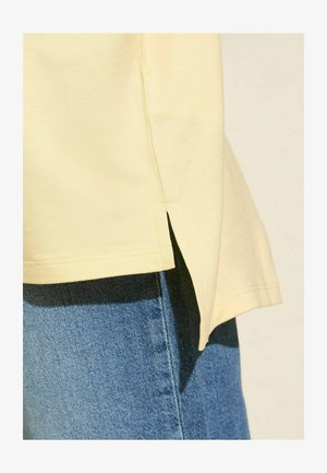 Lichtgele katoenen t-shirt met zijsplitzoom en korte mouwen, gecombineerd met blauwe denim jeans met een gladde textuur en contrasterende stiksels.