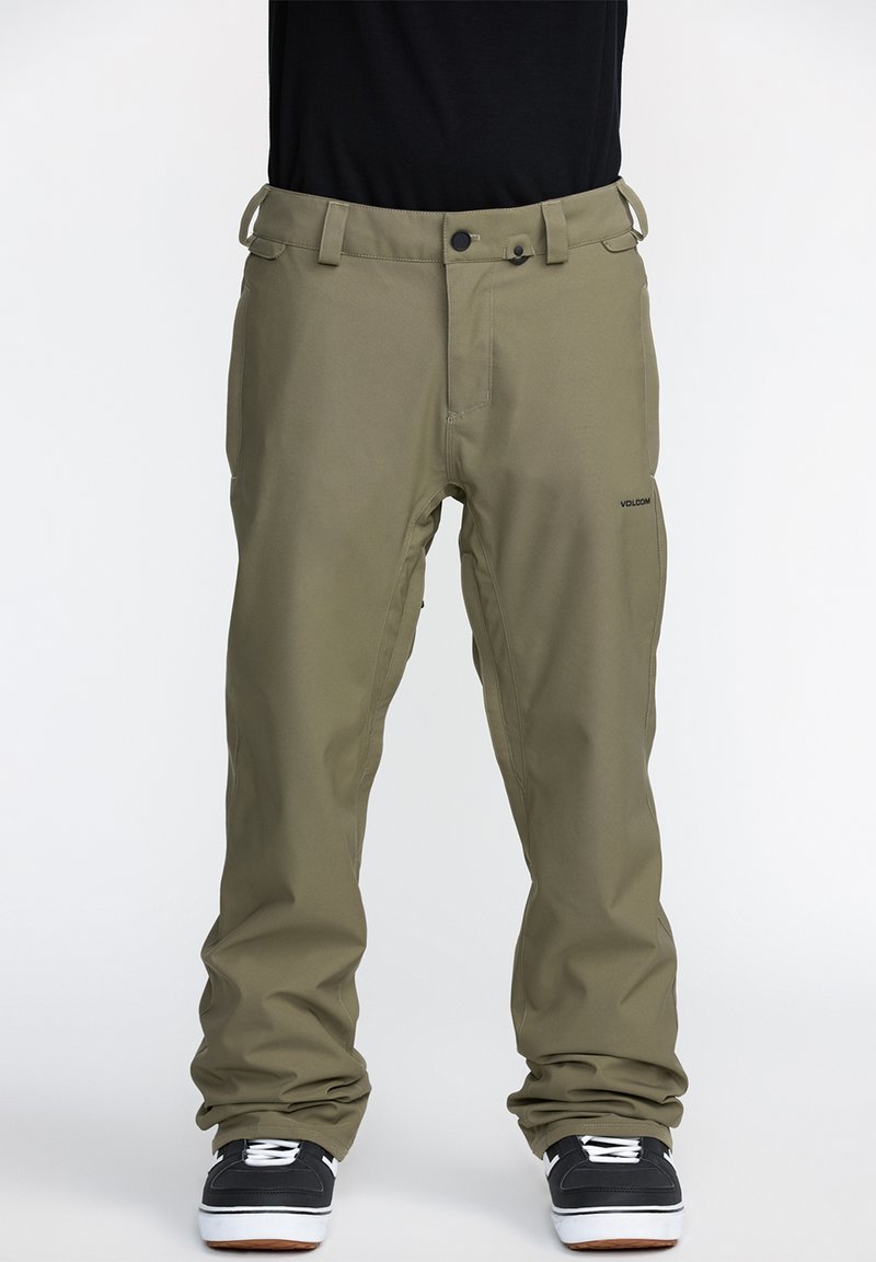 Pantalons de neige vert olive au design droit, avec passants de ceinture, poches avant et un logo de marque discret sur la cuisse. Chaussures noires texturées visibles.