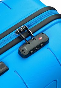 Blauer Hartschalenkoffer mit strukturierter Oberfläche, ausgestattet mit einem schwarzen Reißverschluss, TSA-Schloss und Kombinationsziffernrad; abgerundete Kanten für ein ergonomisches Handling.