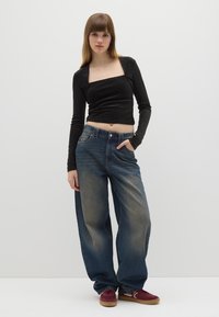 Schwarzes, geripptes, langärmliges Crop-Top mit quadratischem Ausschnitt, kombiniert mit hellen, weit geschnittenen Jeans und burgunderroten Sneakern.