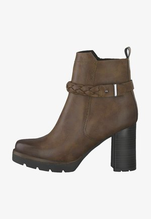 Bota tobillo marrón hecha de material sintético, con una correa trenzada y herrajes plateados, con un tacón grueso y suela texturizada.