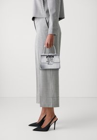 Sac à main argenté avec un design structuré et une poignée supérieure, associé à un costume à carreaux gris et blanc et des escarpins noirs.