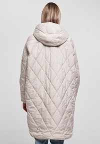 Quiltet beige lang frakk med en oversized hette, med diamantmønstre, vide ermer og en lett buet nederkant bak.
