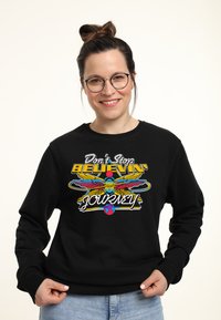 Felpa nera con un design grafico colorato che presenta il testo "Don't Stop Believin'" e un uccello con le ali. Tessuto morbido e casual.