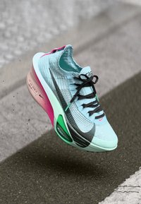 Světle modrá sportovní bota s pleteným svrškem, černým logem swoosh, růžovými a zelenými detaily, tlumením Air Zoom a černými tkaničkami.