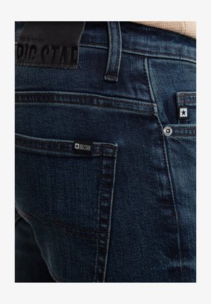 Jeans in denim blu scuro con una finitura testurizzata, cuciture in evidenza e un'etichetta in pelle nera in vita. Due tasche posteriori.