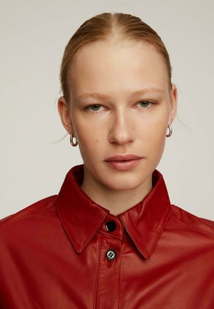 Chaqueta de cuero rojo con cuello de camisa y cierre de botones. Textura suave, presenta dos botones negros y un diseño minimalista.