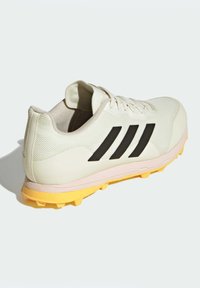 Vit sportskor med svarta tre ränder, texturerad ovandel, vadderad krage och en gul skosula med dobbar. Lätt och hållbar design.