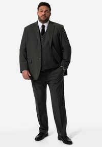 Grau maßgeschneiderter Dreiteiler mit Reverskragen, passender Weste und langen Hosen. Eine schwarze Krawatte und Schuhe runden den Look ab.