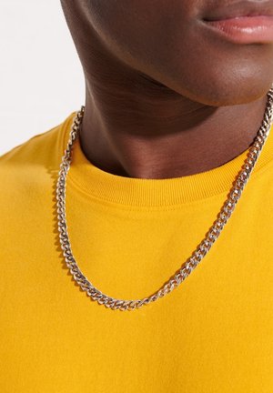 Silver chain necklace with interlocking links, worn over a bright yellow shirt featuring a ribbed crew neckline.