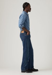 Πουκάμισο από τζιν σε ανοιχτό μπλε, συνδυασμένο με σκούρα μπλε καμπάνα τζιν παντελόνια. Φορεμένο με μαύρα μποτάκια. Περιλαμβάνει κλασικό γιακά και μπροστινές τσέπες.