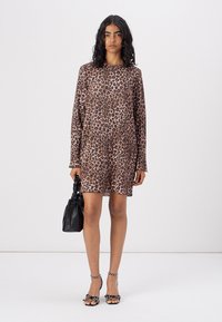 Šaty s leopardím potiskem, dlouhý rukáv, měkký materiál, volný střih, délka nad kolena, doplněné černou kabelkou a zdobenými sandály.