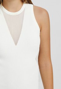 Débardeur blanc côtelé avec un panneau triangulaire transparent au niveau du col, design sans manches et texture lisse.