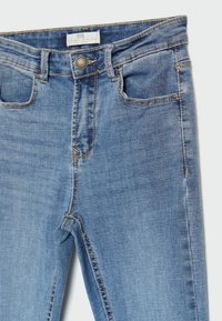 Vaqueros de mezclilla azul claro con un diseño ajustado, cinco bolsillos y herrajes en tono cobre con costuras visibles.