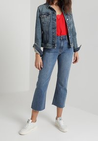 Giacca di jeans blu scuro, top rosso con pizzo, jeans cropped a vita alta e sneakers bianche. Presenta tasche e orlo sfilacciato.