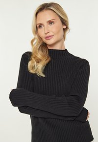 Schwarzer gerippter Strickpullover mit hohem Kragen und langen Ärmeln, der eine weiche Textur und eine figurbetonte Form aufweist, ideal zum Layering.