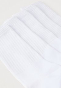 Hvide ribstrikkede sokker med en blød tekstur og elastiske manchetter, designet for komfort, med en glat finish uden mønstre eller accenter.