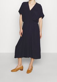 Navy v-hals midi kjole med løse ærmer og elastisk talje. Gulvlængde med glat tekstur. Brune vævede lavhælede sko.