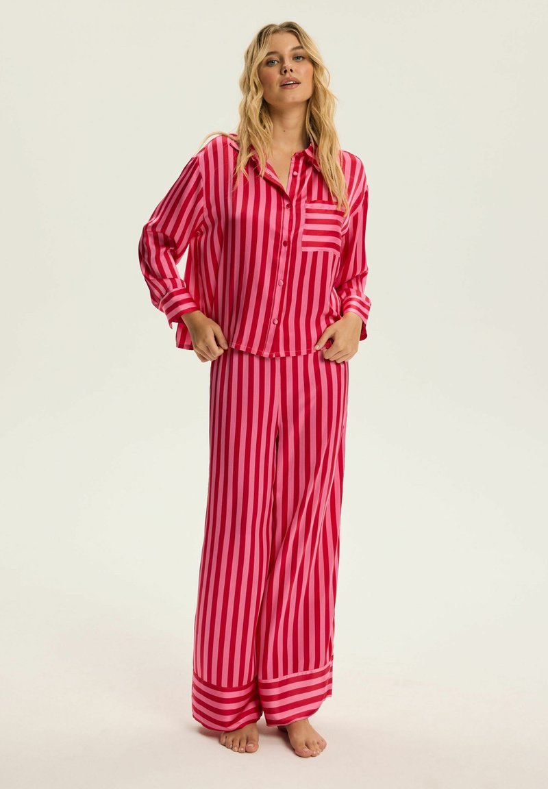 Różowy i fuksjowy zestaw piżamowy w paski, składający się z koszuli zapinanej na guziki z kieszonką oraz luźnych spodni z szerokimi nogawkami i mankietami.