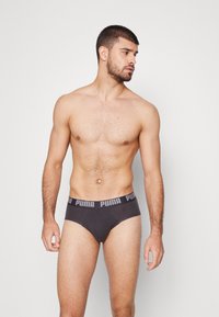 Grau Unterwäsche mit einem breiten schwarzen Bund, der das "PUMA"-Logo trägt. Der Stoff wirkt glatt und hat einen enganliegenden Schnitt, der sich gut für Sportaktivitäten eignet.